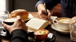 a photo of a table with coffee, pastries, and one person taking notes